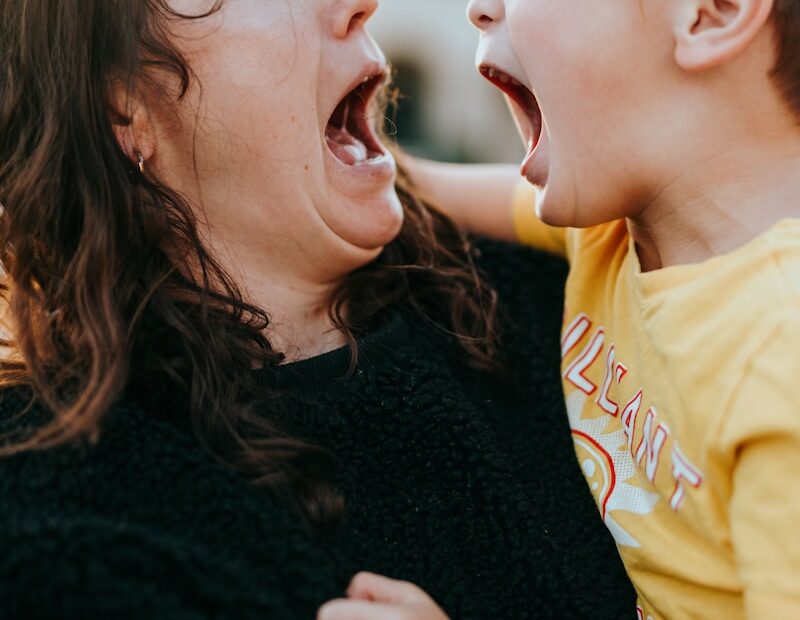 woman in black sweater kissing girl in yellow shirt